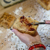 Lemon Curd and Strawberry Pepper Jam being spread on a Bacon Fat Biscuit over a bakers bench with flour.