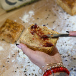 Lemon Curd and Strawberry Pepper Jam being spread on a Bacon Fat Biscuit over a bakers bench with flour.