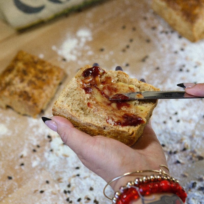 Lemon Curd and Strawberry Pepper Jam being spread on a Bacon Fat Biscuit over a bakers bench with flour.